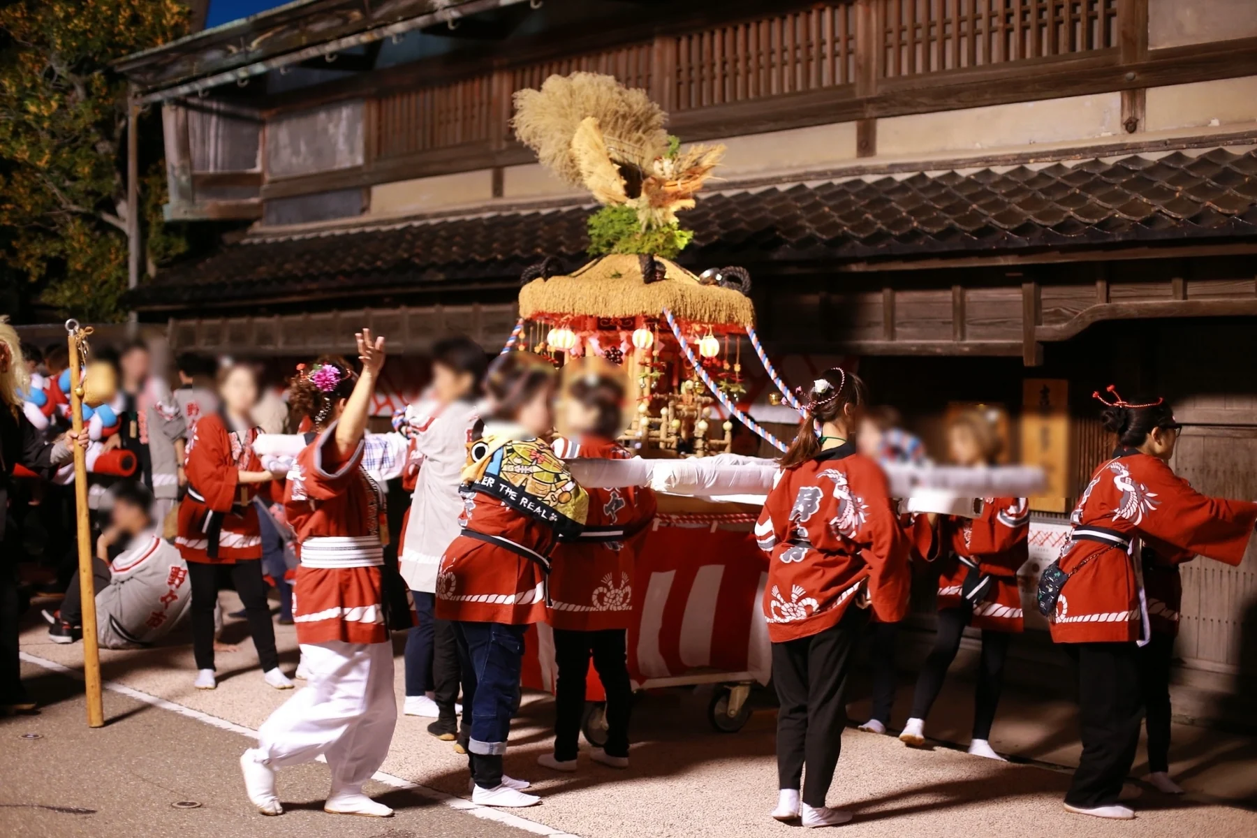 夜の北国街道で女性が豊年野菜神輿を囲む様子